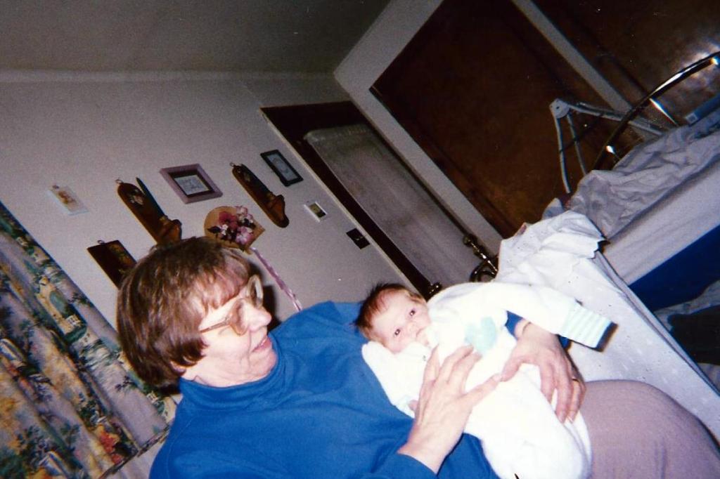 Grandma holding Carly in the Savona house. The top of the swing is visible in the background.
